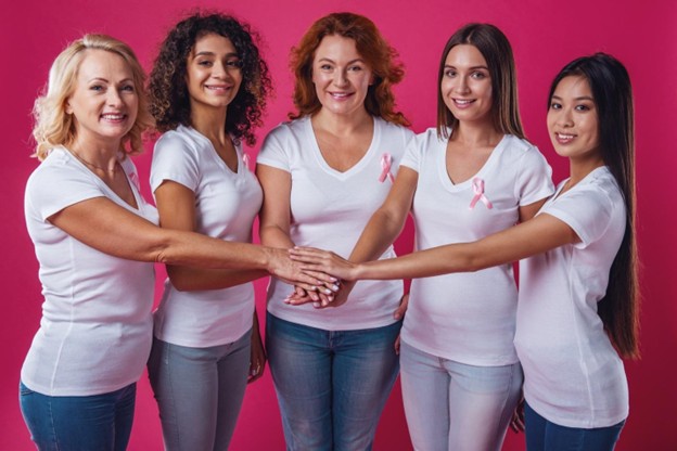 Mujeres uniendo las manos con un lazo rosado en sus camisas.
