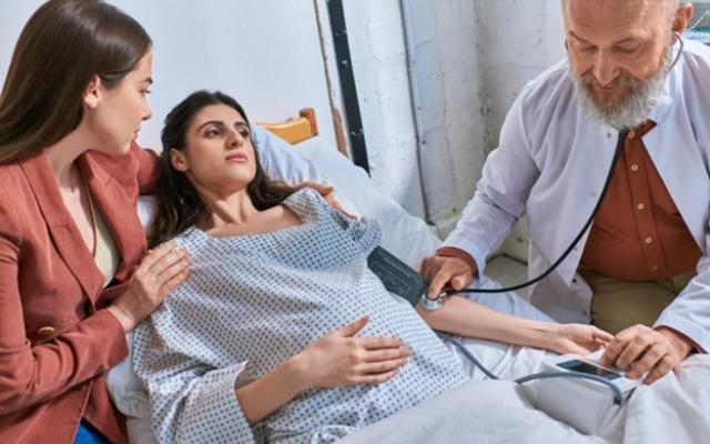 Paciente que luce un poco enferma, siendo examinada por un doctor mientras una familiar la acompaña.